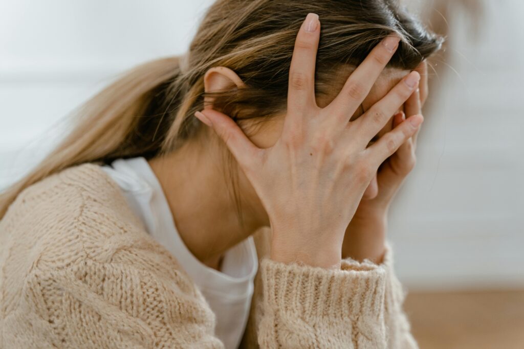 pexels-photo-7699410-7699410 Woman sitting indoors with face covered by hands, expressing stress and frustration.