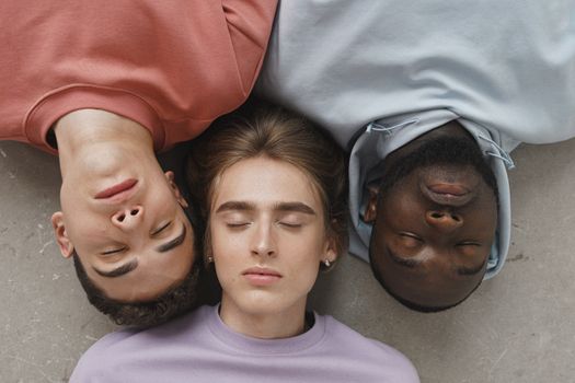 pexels-photo-9775887-9775887 Three diverse young adults with eyes closed, lying on the ground wearing pastel hoodies.